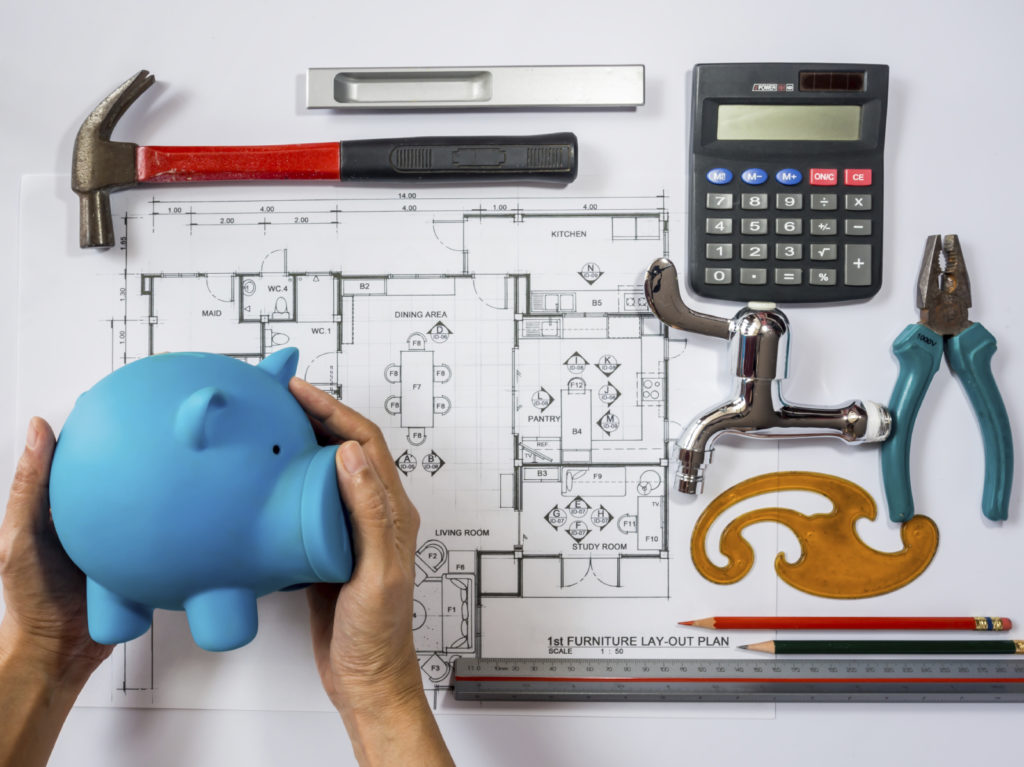 Hands holding piggy bank over architecture drawing, planning for home remodel / saving concept